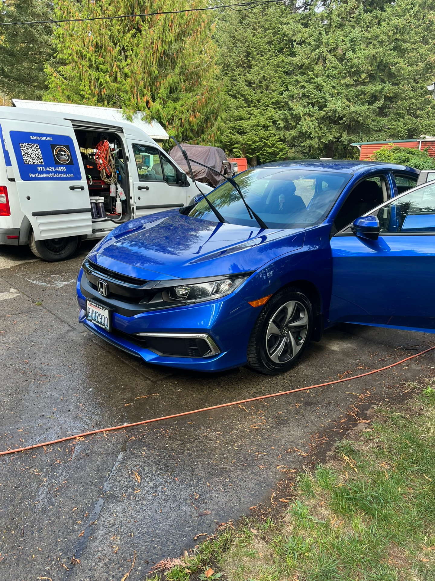 Blue Honda with open doors beside a mobile detailing van